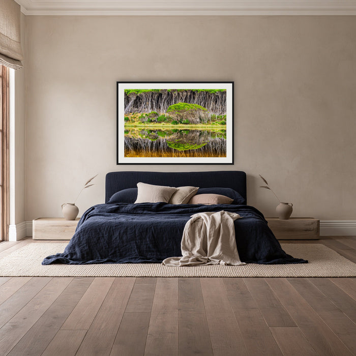 Bournda Lagoon Reflections framed print in black with a white mat, above a navy linen bed in a bedroom