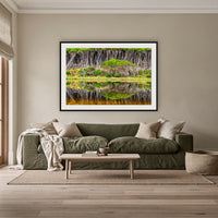 Bournda Lagoon Reflections framed print in black with a white mat, above an olive linen sofa in a lounge room
