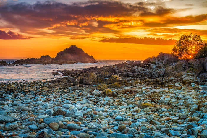 Sunrise burning orange behind a rocky island at Mimosa Rocks, rounded pale boulders filling the foreground — fine art print