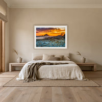 Mimosa Rocks Sunrise framed print in oak with a white mat, above an oatmeal linen bed in a bedroom