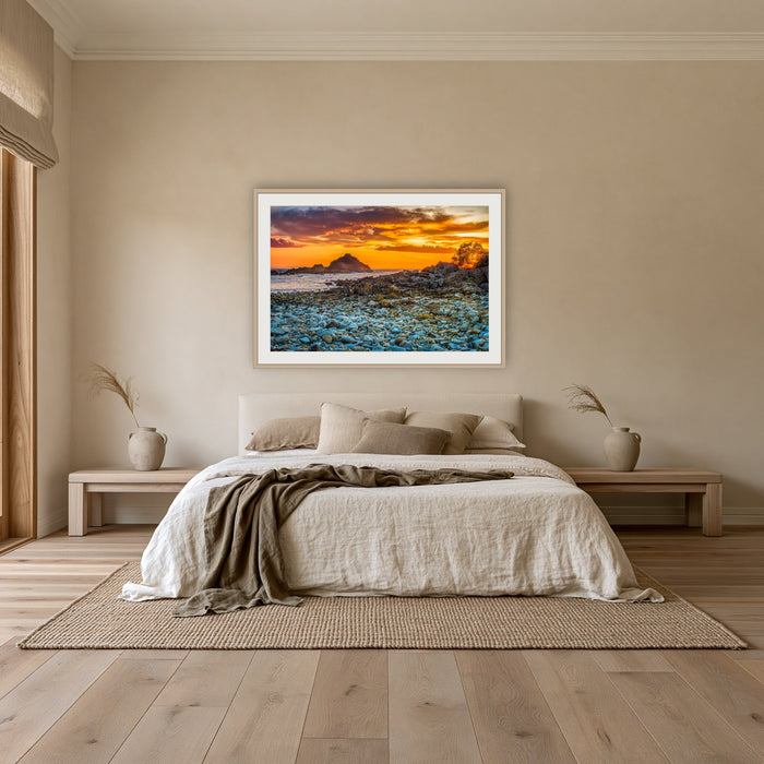 Mimosa Rocks Sunrise framed print in oak with a white mat, above an oatmeal linen bed in a bedroom