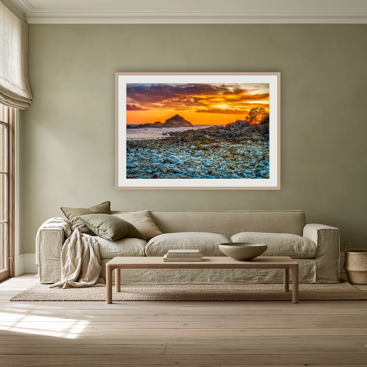 Mimosa Rocks Sunrise framed print in oak with a white mat, above a linen sofa against a sage wall in a lounge room