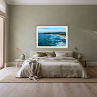 Cuttagee Beach framed print in oak with a white mat, above a linen bed against a sage wall in a bedroom