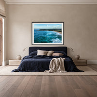 Cuttagee Beach framed print in black with a white mat, above a navy linen bed in a bedroom