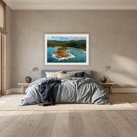 Mimosa Rocks framed print in oak with a white mat, above a dusty blue linen bed in a bedroom