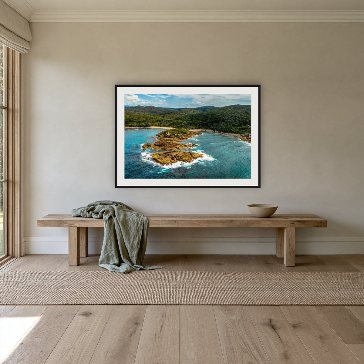 Mimosa Rocks framed print in black with a white mat, above an oak bench in a hallway