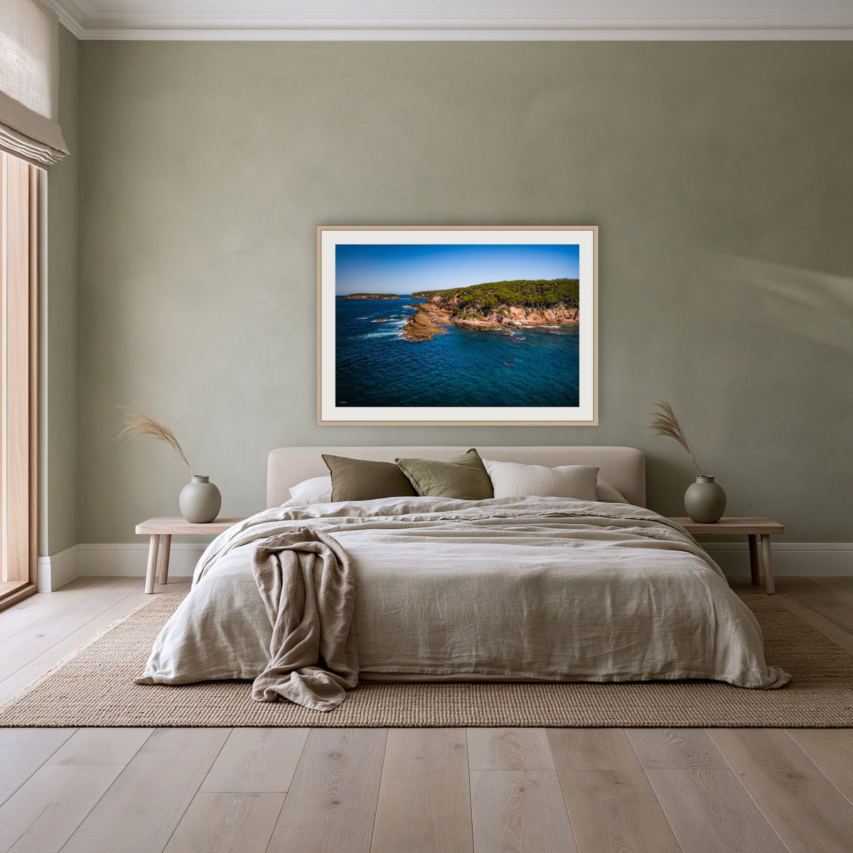 Terrace Beach framed print in oak with a white mat, above a linen bed against a sage wall in a bedroom