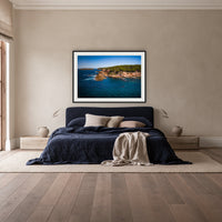 Terrace Beach framed print in black with a white mat, above a navy linen bed in a bedroom