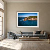 Terrace Beach framed print in oak with a white mat, above a dusty blue linen sofa in a lounge room