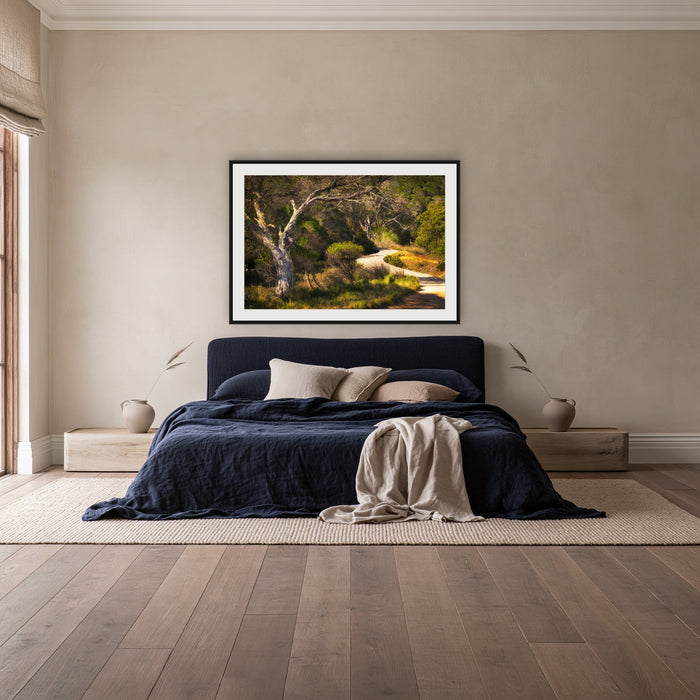 Merimbula Boardwalk framed print in black with a white mat, above a navy linen bed in a bedroom