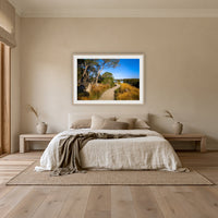Merimbula Boardwalk through Golden Grasses framed print in oak with a white mat, above an oatmeal linen bed in a bedroom