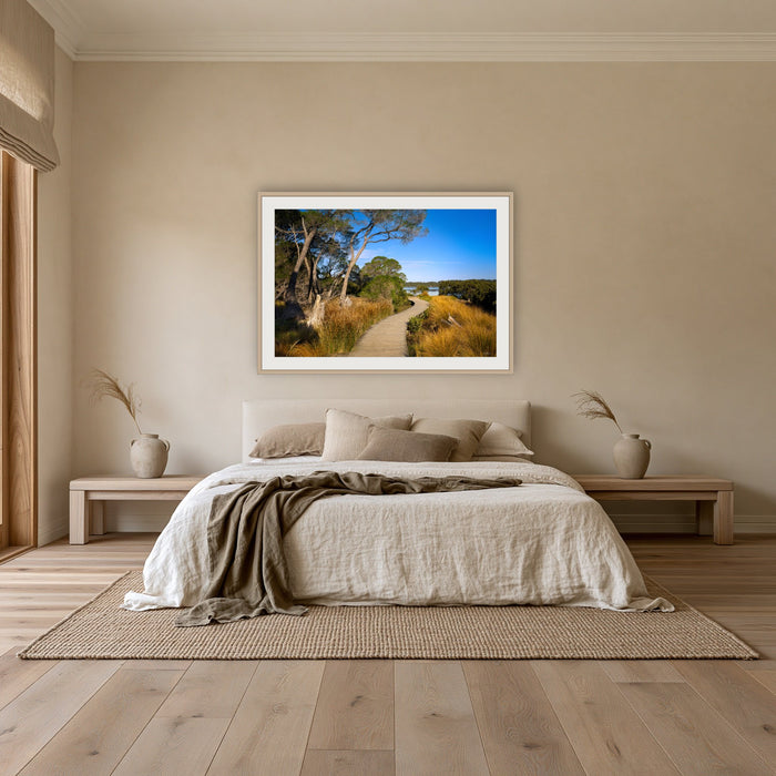 Merimbula Boardwalk through Golden Grasses framed print in oak with a white mat, above an oatmeal linen bed in a bedroom