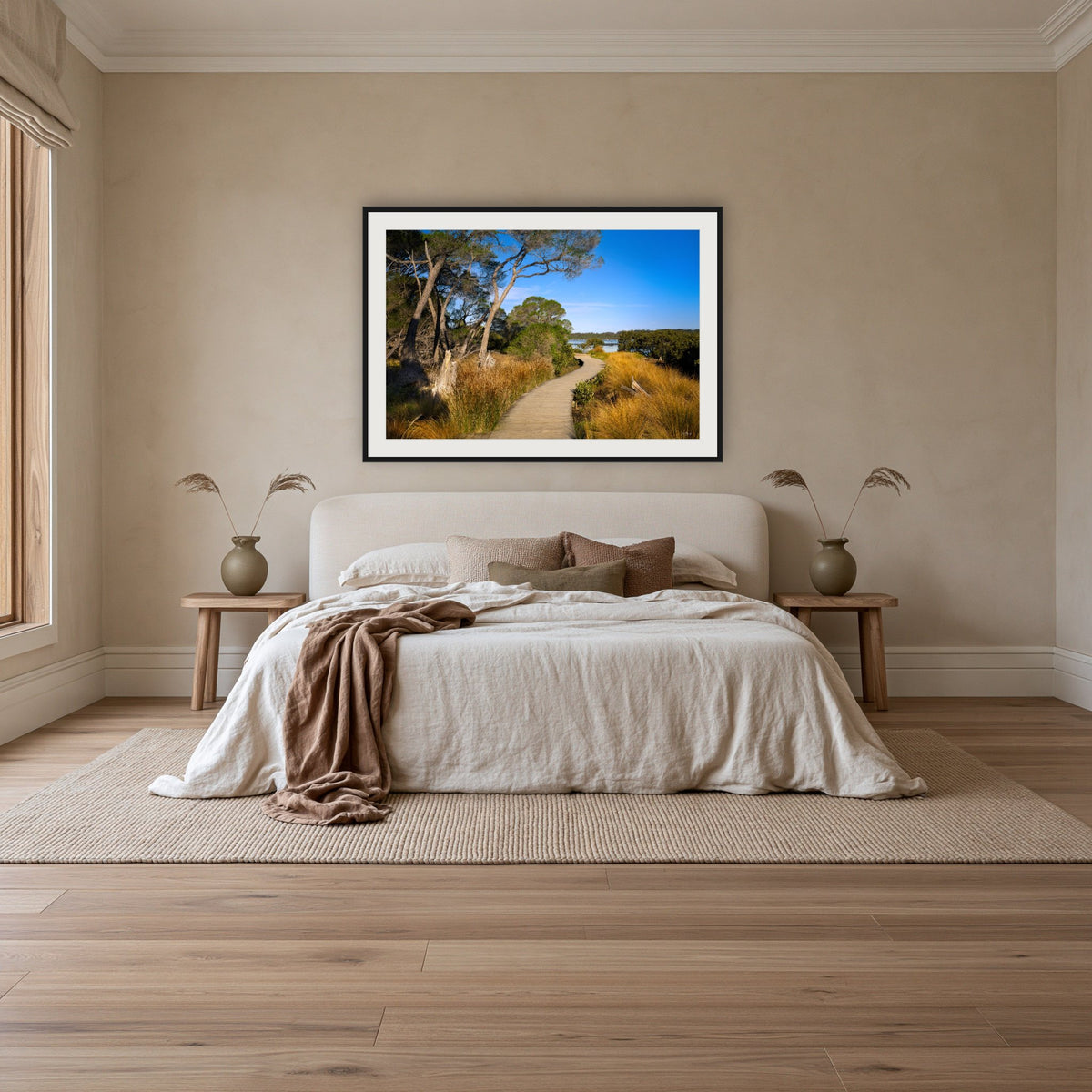 Merimbula Boardwalk through Golden Grasses framed print in black with a white mat, above an ivory linen bed in a bedroom