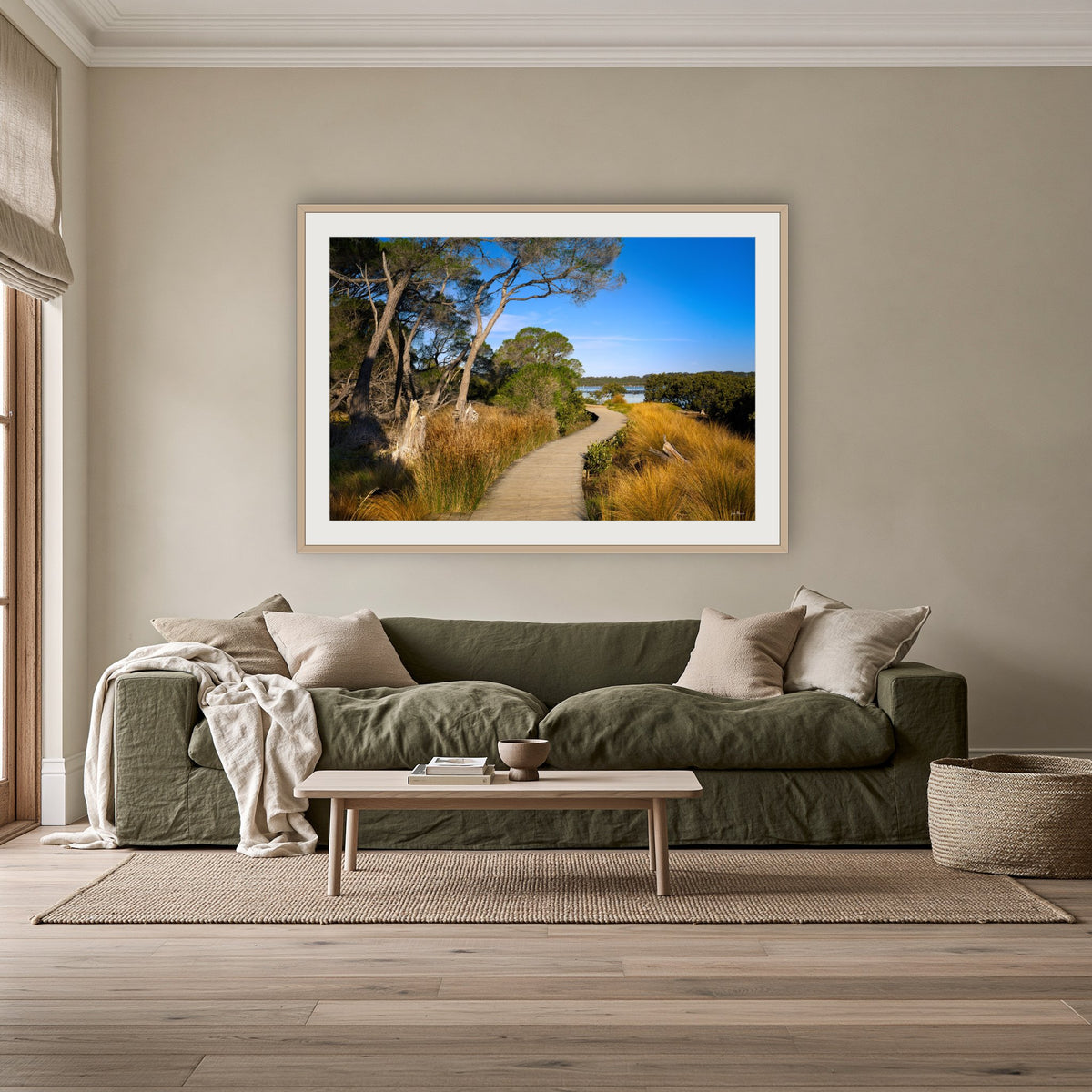 Merimbula Boardwalk through Golden Grasses framed print in oak with a white mat, above an olive linen sofa in a lounge room