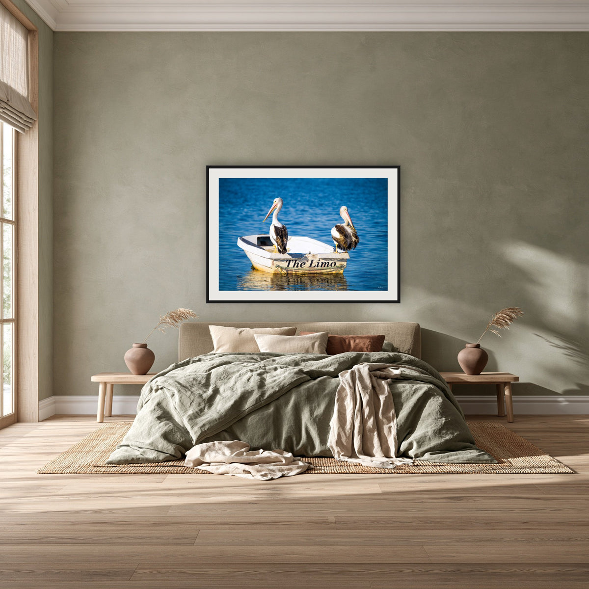 Pelican's Limo framed print in black with a white mat, above a khaki linen bed against a green-grey wall in a bedroom