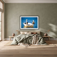 Pelican's Limo framed print in black with a white mat, above a khaki linen bed against a green-grey wall in a bedroom