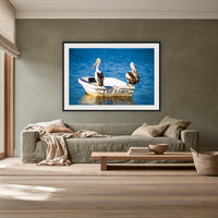 Pelican's Limo framed print in black with a white mat, above a sage linen sofa in a lounge room