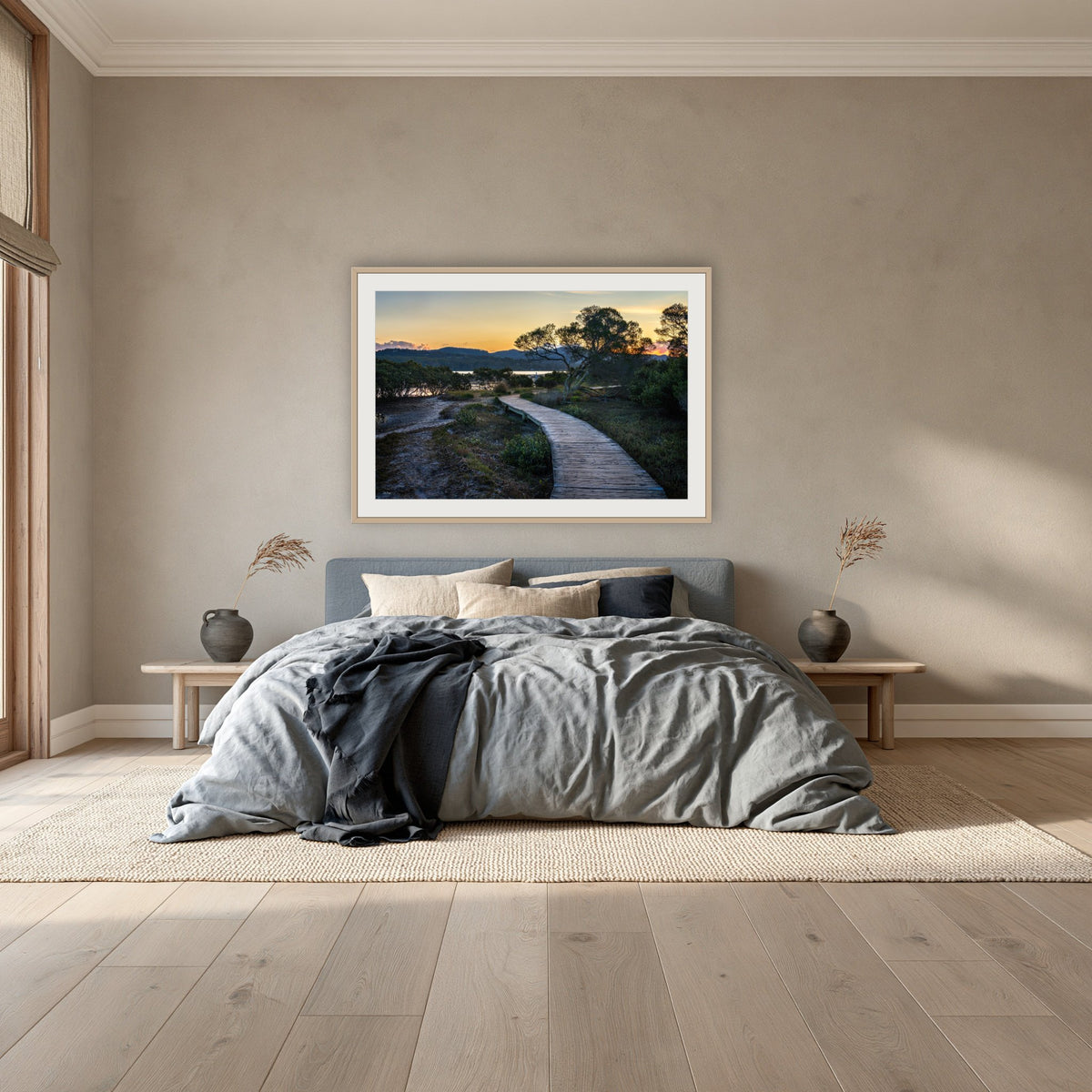 Merimbula Boardwalk at Dusk framed print in oak with a white mat, above a dusty blue linen bed in a bedroom