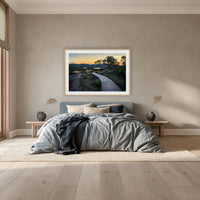 Merimbula Boardwalk at Dusk framed print in oak with a white mat, above a dusty blue linen bed in a bedroom