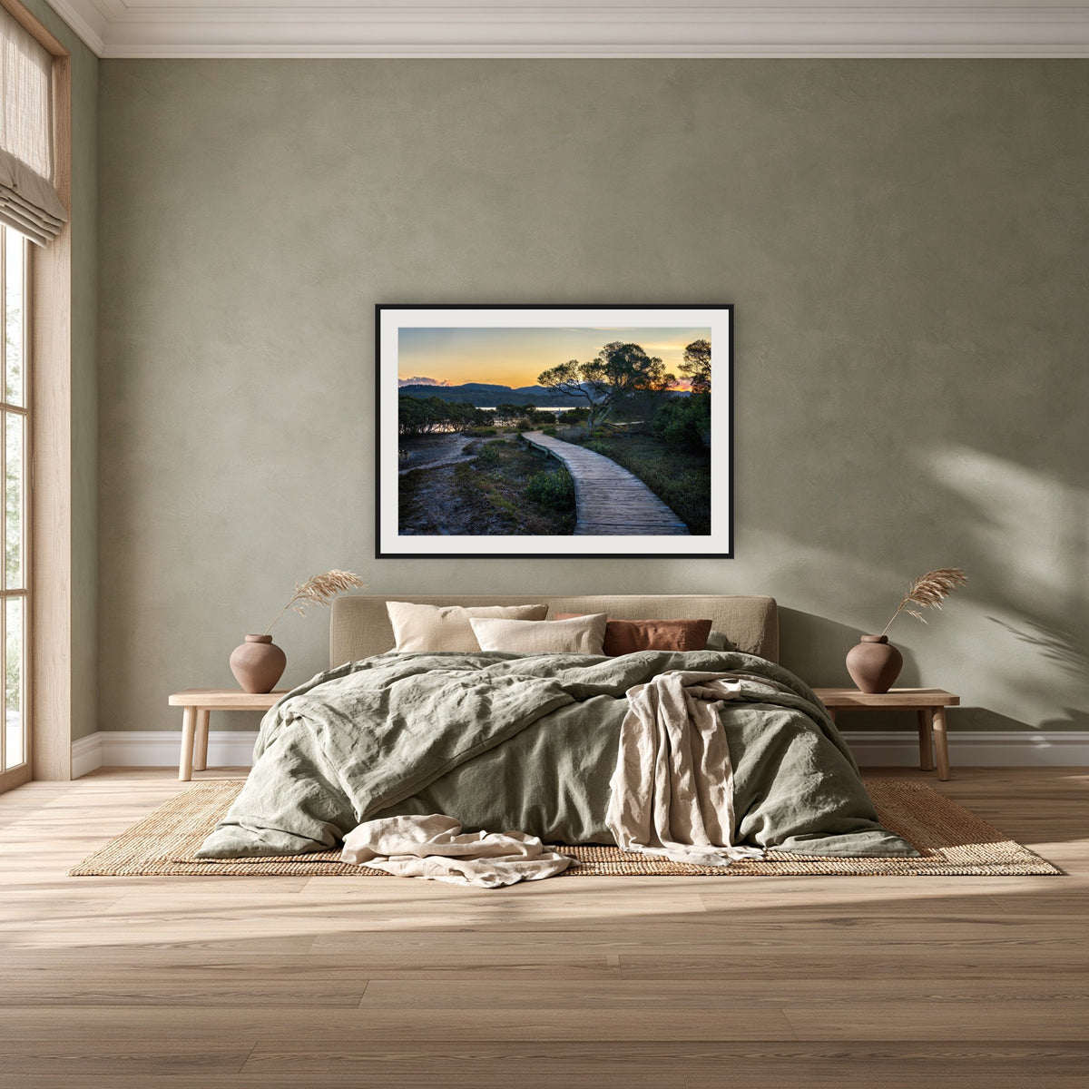 Merimbula Boardwalk at Dusk framed print in black with a white mat, above a khaki linen bed against a green-grey wall in a bedroom