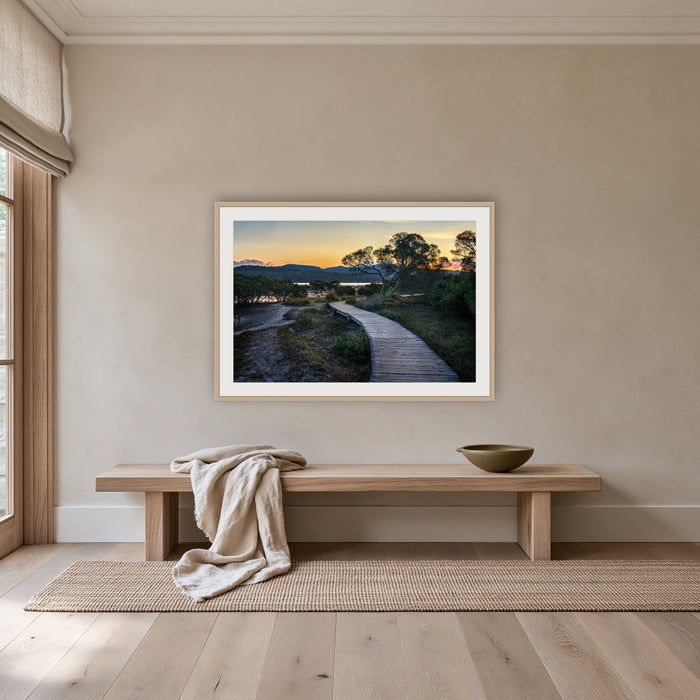 Merimbula Boardwalk at Dusk framed print in oak with a white mat, above an oak bench in a hallway