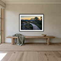 Merimbula Boardwalk at Dusk framed print in black with a white mat, above an oak bench in a hallway