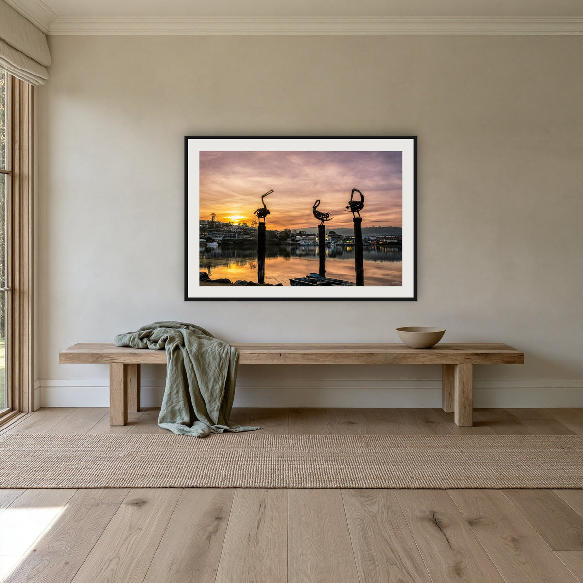 Pelican Sculptures framed print in black with a white mat, above an oak bench in a hallway