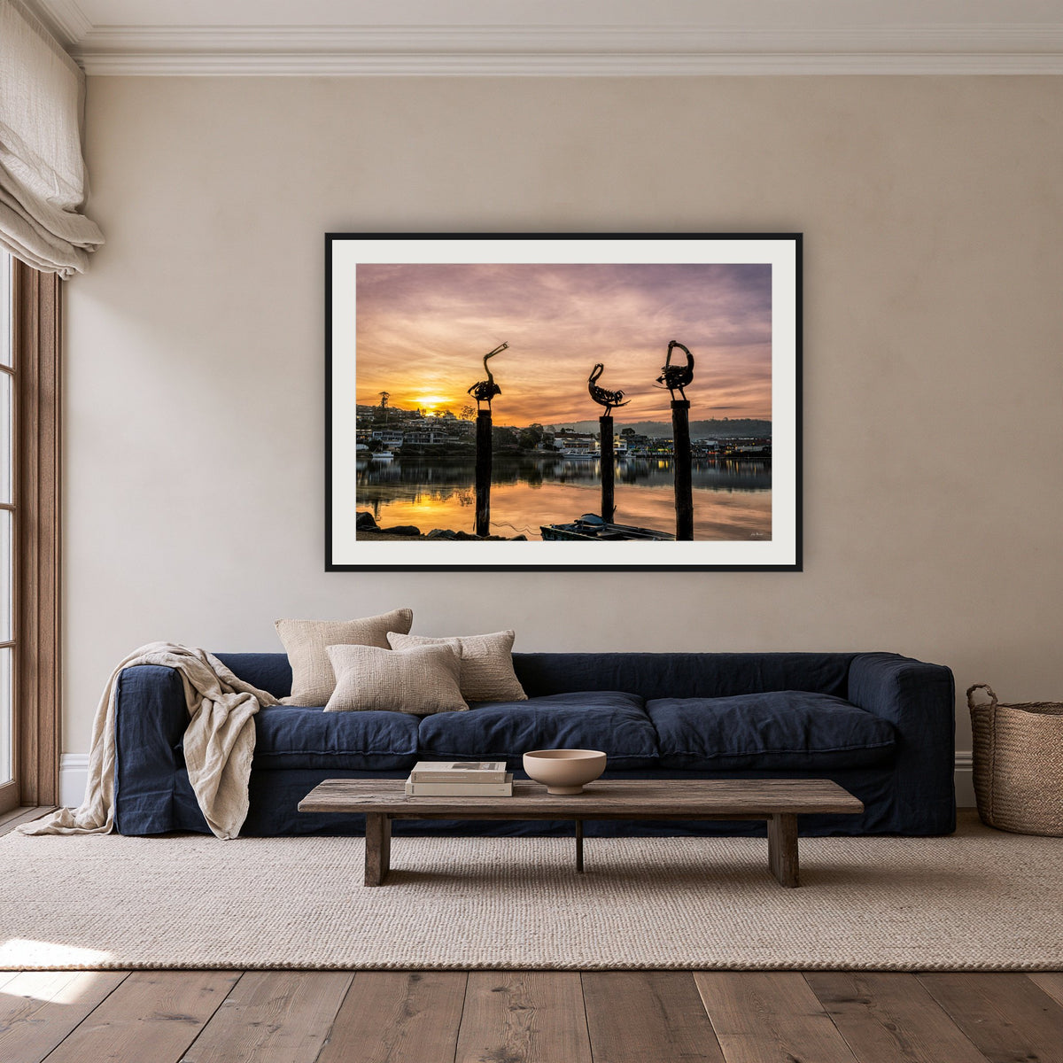 Pelican Sculptures framed print in black with a white mat, above a navy linen sofa in a lounge room