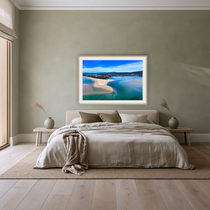 Merimbula Lake and Coastline framed print in oak with a white mat, above a linen bed against a sage wall in a bedroom