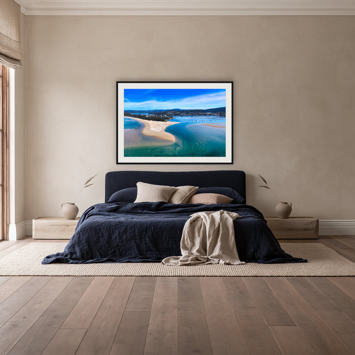 Merimbula Lake and Coastline framed print in black with a white mat, above a navy linen bed in a bedroom