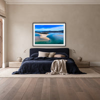 Merimbula Lake and Coastline framed print in black with a white mat, above a navy linen bed in a bedroom