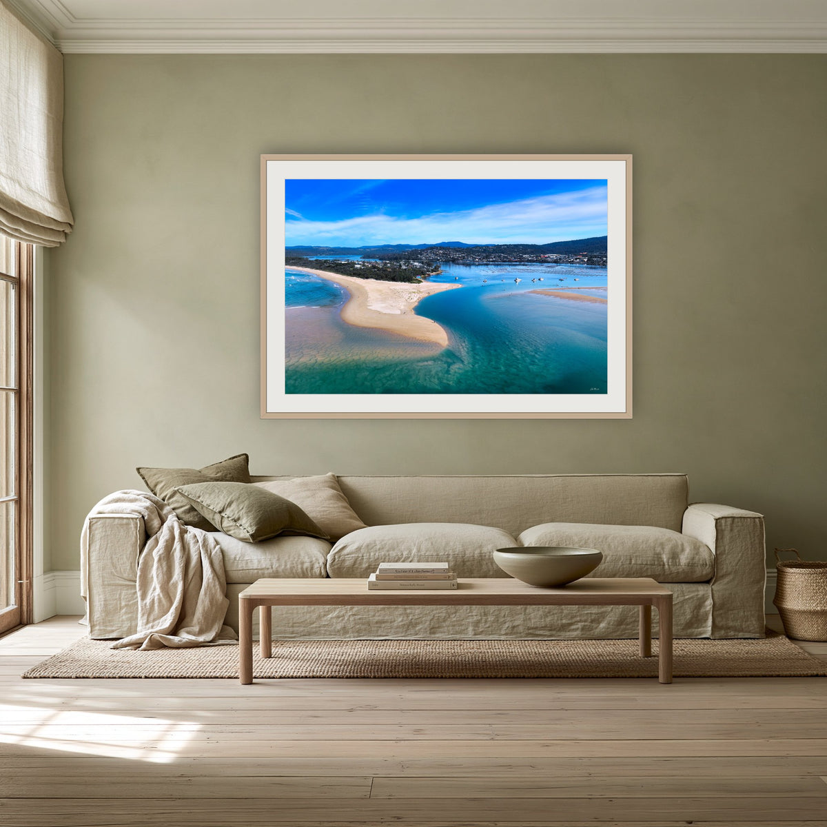 Merimbula Lake and Coastline framed print in oak with a white mat, above a linen sofa against a sage wall in a lounge room