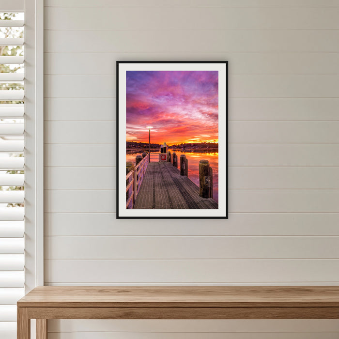 Sunrise over Merimbula Lake framed print in black with a white mat, in a shiplap hallway