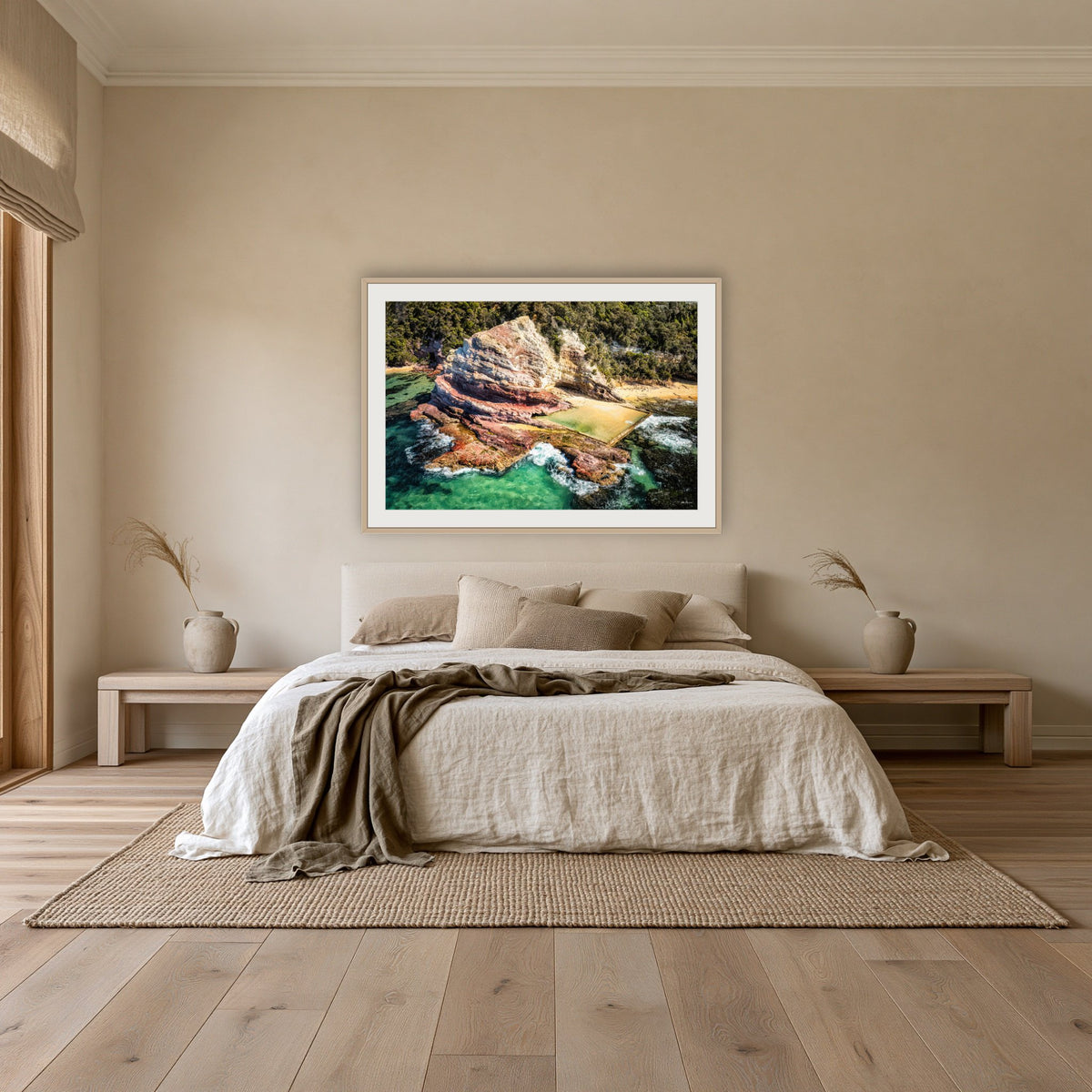 Aslings Beach Rock Pool framed print in oak with a white mat, above an oatmeal linen bed in a bedroom