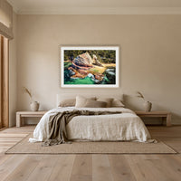 Aslings Beach Rock Pool framed print in oak with a white mat, above an oatmeal linen bed in a bedroom