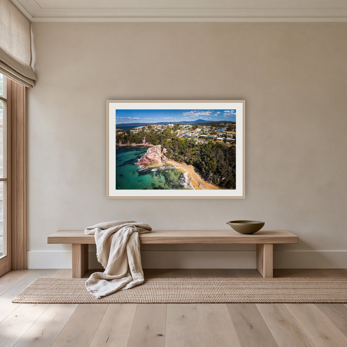 Aslings Beach from the Air framed print in oak with a white mat, above an oak bench in a hallway