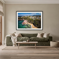 Aslings Beach from the Air framed print in black with a white mat, above an olive linen sofa in a lounge room