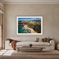 Aslings Beach from the Air framed print in oak with a white mat, above an oatmeal linen sofa in a lounge room