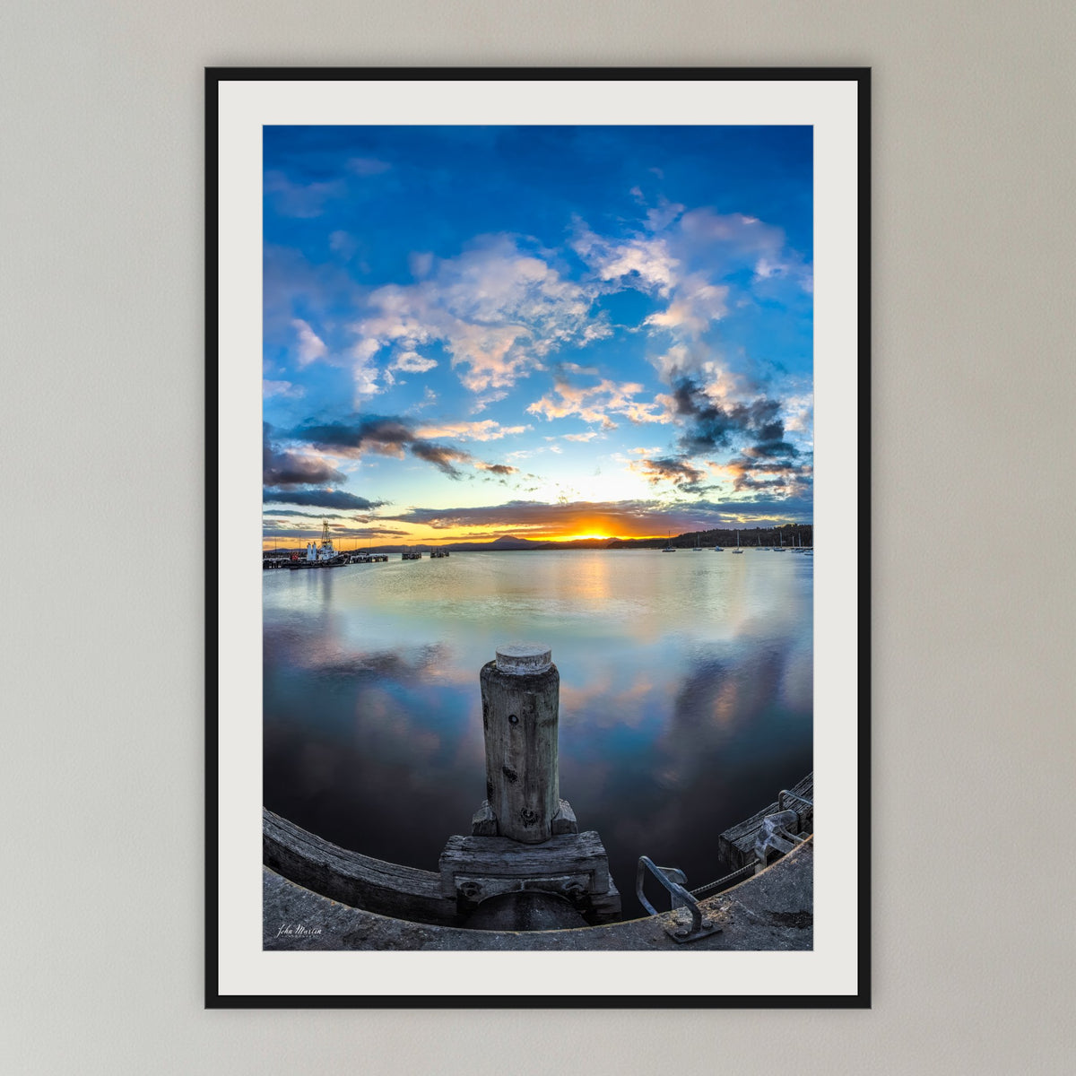 Eden Wharf Sunset framed print in black with a white mat, in a cane-panelled hallway