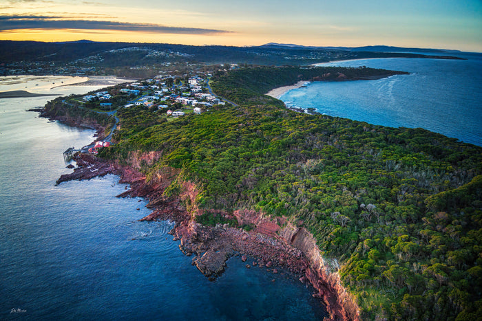 Aerial view along the forested Long Point headland at Merimbula, red cliffs falling to the sea on one side and the beach curving away on the other — fine art print