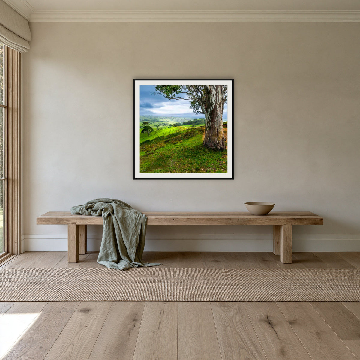 Bega Valley Countryside square framed print in black with a white mat, above a timber bench in a hallway