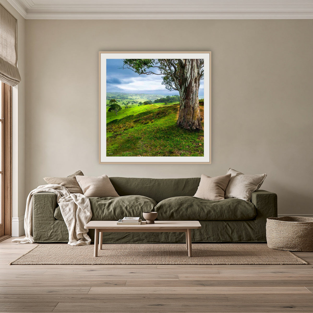 Bega Valley Countryside square framed print in oak with a white mat, above an olive linen sofa in a lounge room