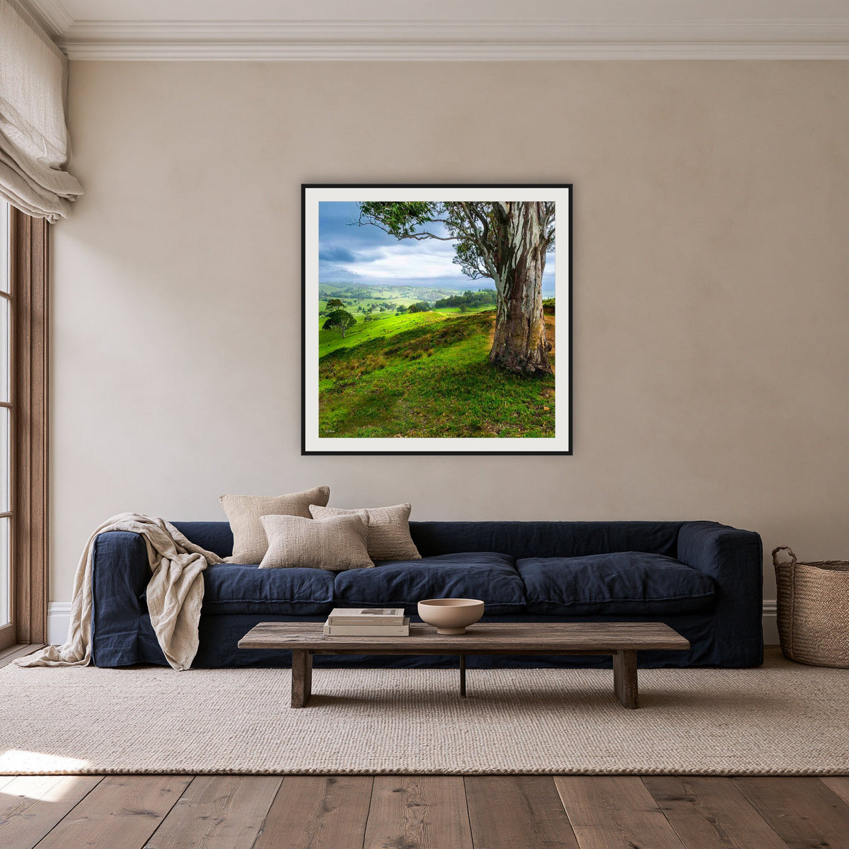 Bega Valley Countryside square framed print in black with a white mat, above a navy linen sofa in a lounge room