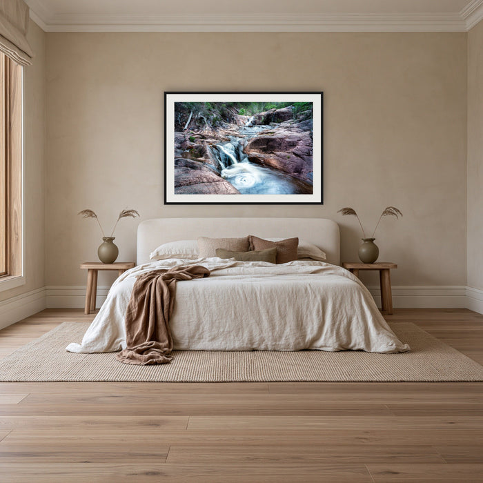 Biamanga Cultural Area framed print in black with a white mat, above an ivory linen bed in a bedroom