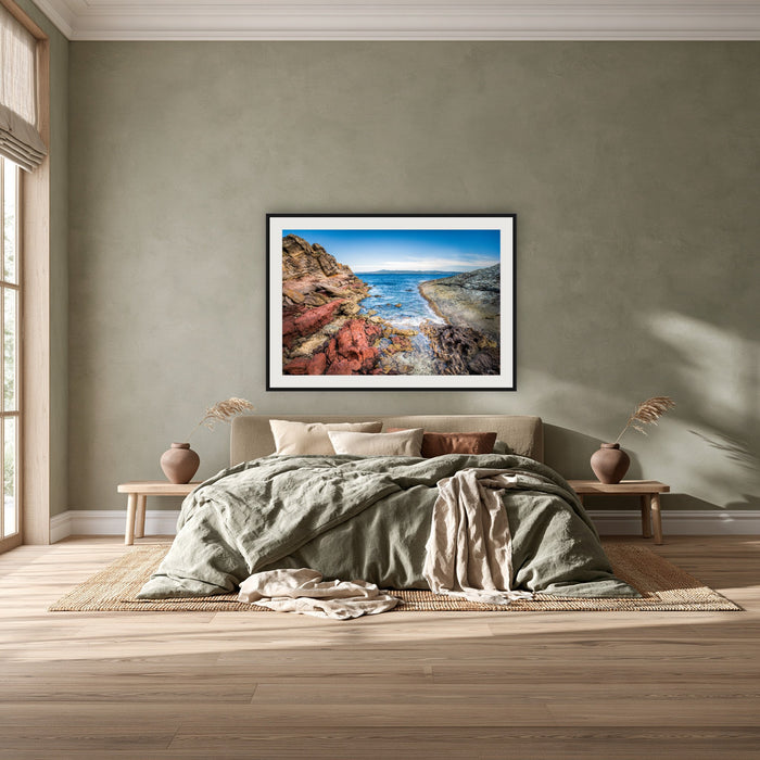 North Head Worang Point framed print in black with a white mat, above a khaki linen bed against a green-grey wall in a bedroom