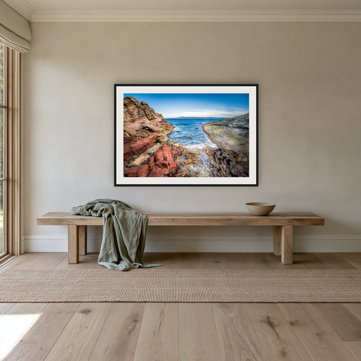 North Head Worang Point framed print in black with a white mat, above an oak bench in a hallway