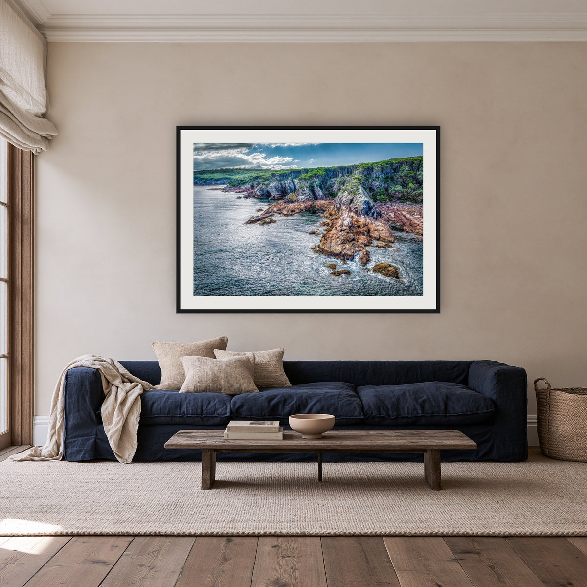North Head Worang Point Headland framed print in black with a white mat, above a navy linen sofa in a lounge room