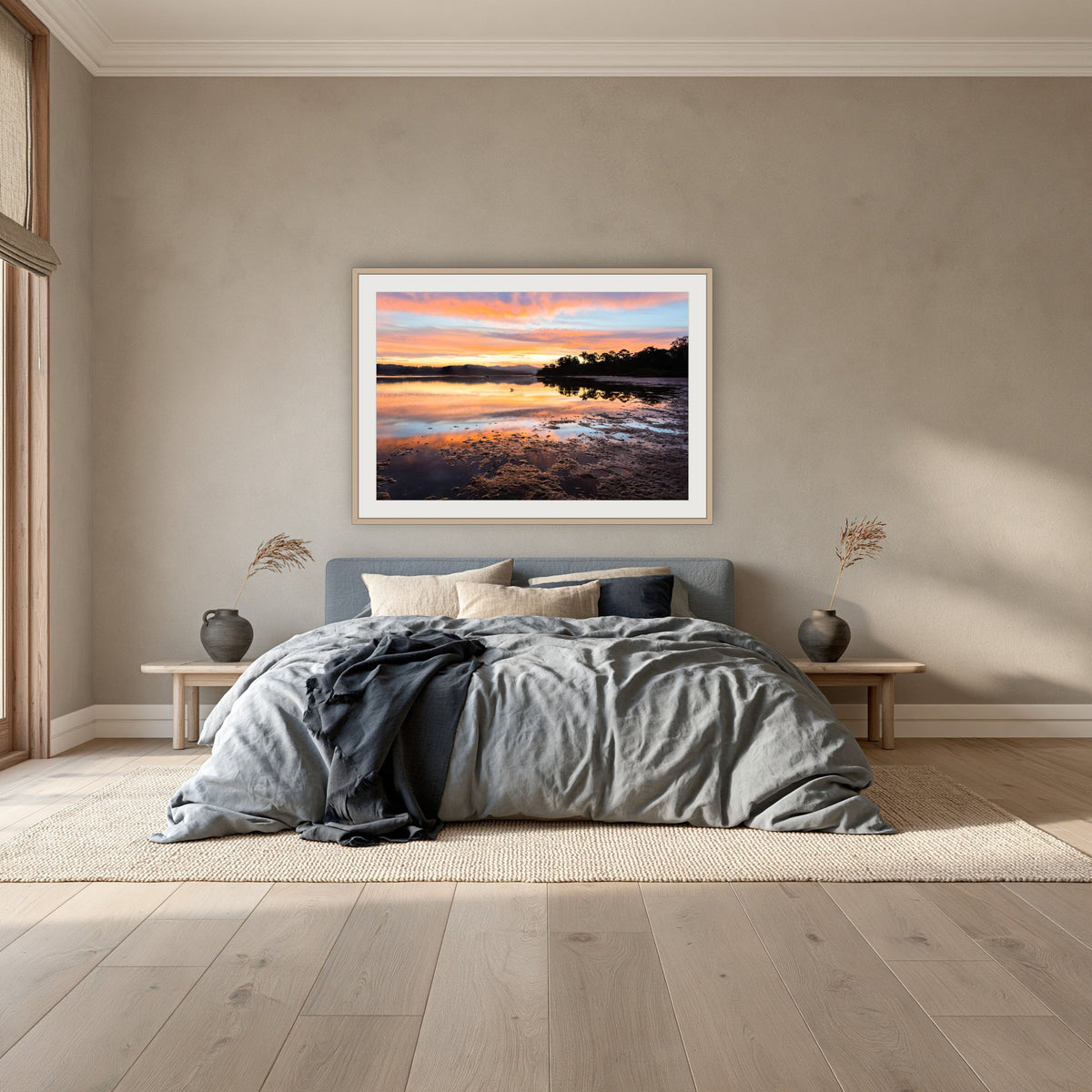Top Lake Sunset framed print in oak with a white mat, above a dusty blue linen bed in a bedroom