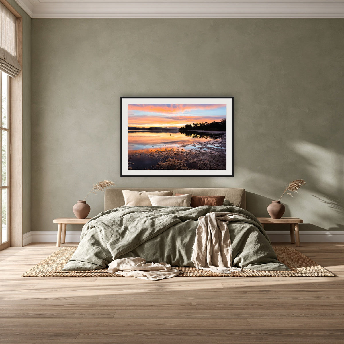 Top Lake Sunset framed print in black with a white mat, above a khaki linen bed against a green-grey wall in a bedroom