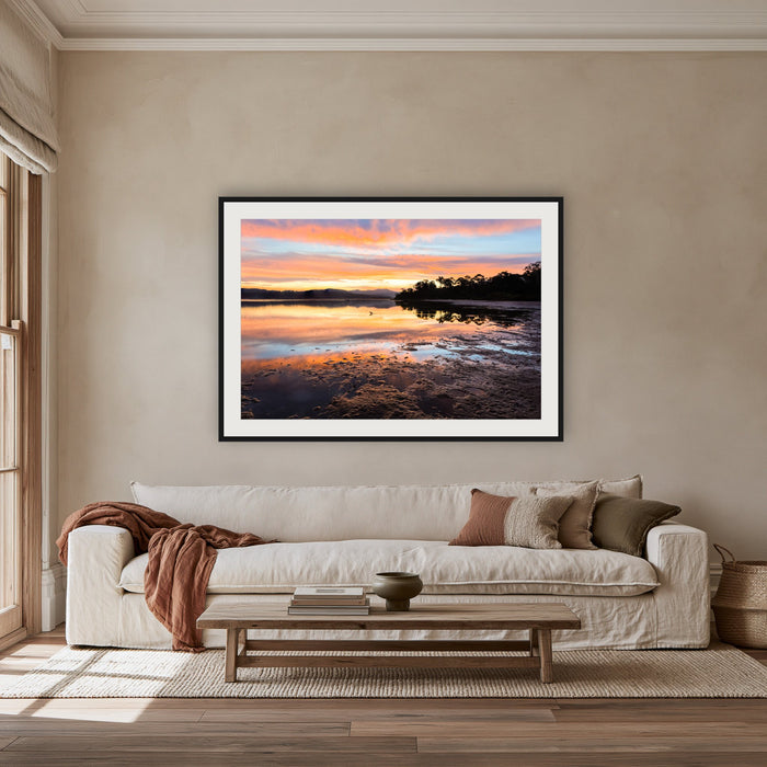 Top Lake Sunset framed print in black with a white mat, above an oatmeal linen sofa in a lounge room